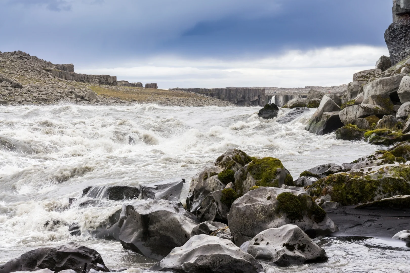une côte rocheuse avec des vagues qui s'écrasent contre des rochers noirs, sous un ciel gris